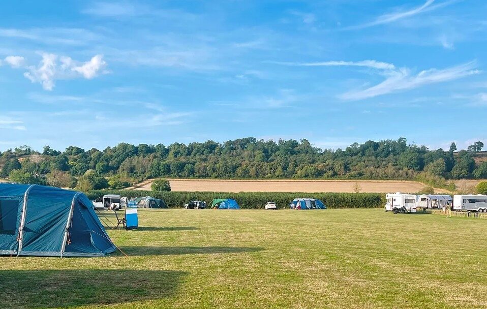 Tents pitched on the open grass field with wooded hills behind