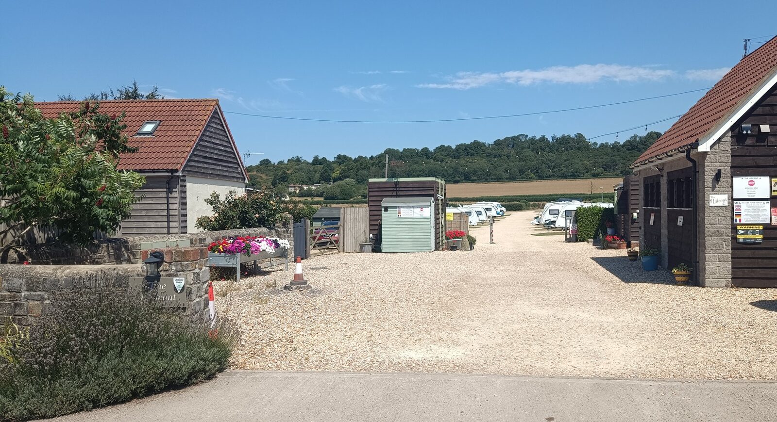 The gravel entrance to The Hideout on a sunny day, with pitches and wooded hills beyond