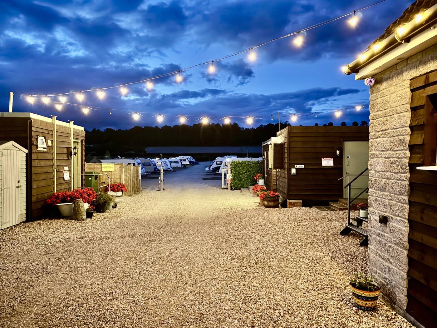The site entrance at dusk, festoon lights strung above the gravel and caravans beyond