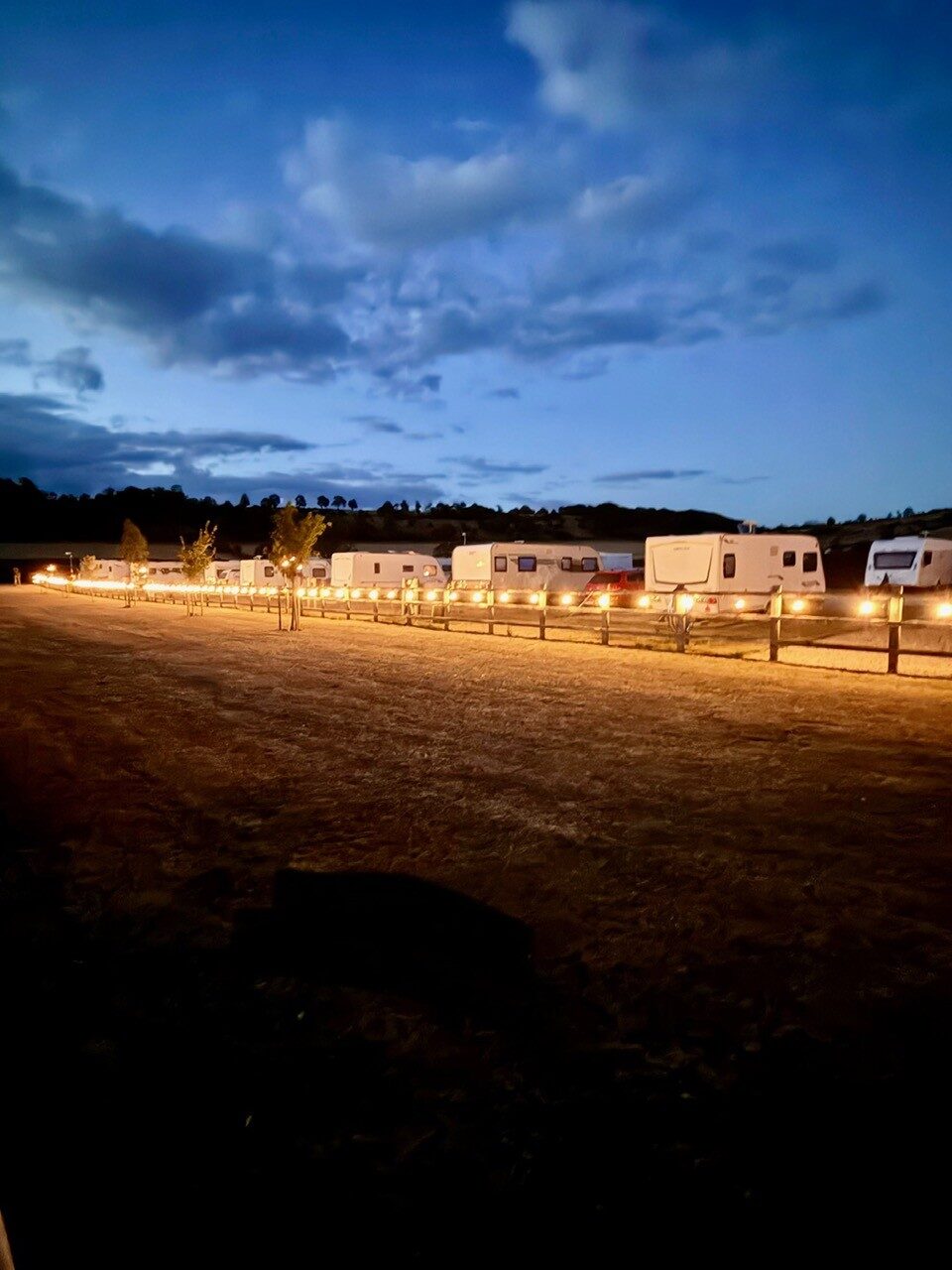 The touring field at night, warm lights running along the fence line